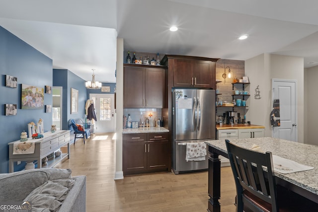 kitchen featuring light wood finished floors, decorative backsplash, an inviting chandelier, freestanding refrigerator, and dark brown cabinetry