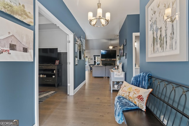 foyer entrance featuring ceiling fan with notable chandelier, vaulted ceiling, a fireplace, and wood finished floors