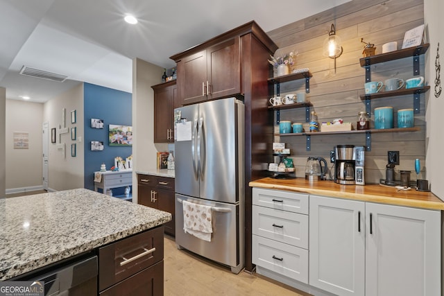 kitchen with light stone counters, visible vents, dark brown cabinets, freestanding refrigerator, and open shelves