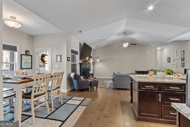 dining room featuring a fireplace, lofted ceiling, visible vents, light wood-style floors, and baseboards