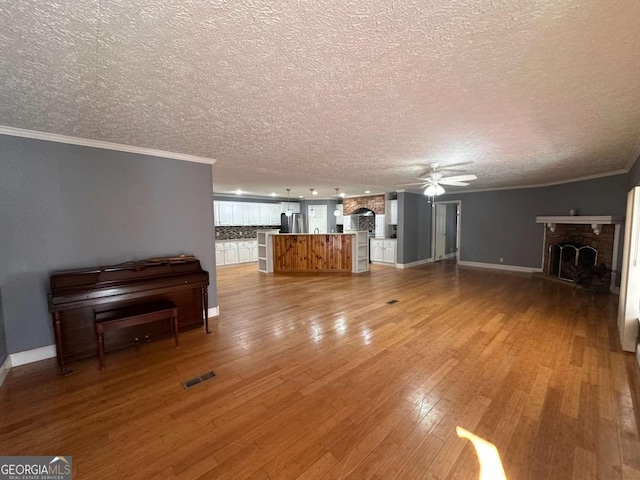 unfurnished living room featuring ornamental molding, a fireplace with raised hearth, ceiling fan, and light wood finished floors