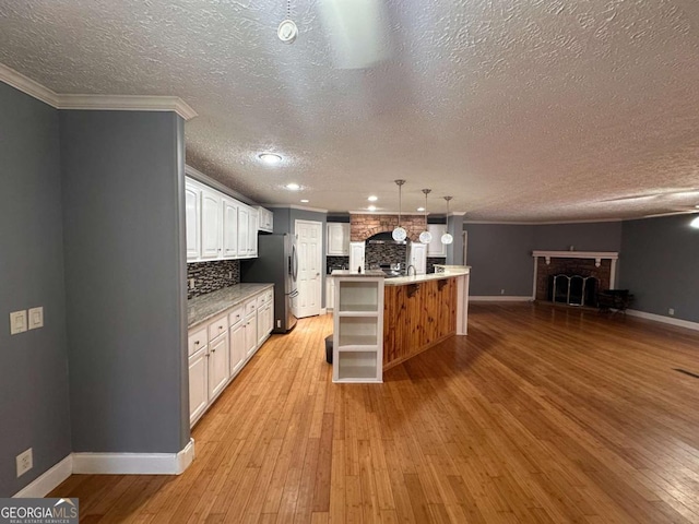 kitchen with light wood finished floors, freestanding refrigerator, a brick fireplace, white cabinets, and open floor plan