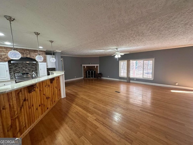 unfurnished living room featuring a fireplace, hardwood / wood-style floors, ornamental molding, ceiling fan, and baseboards