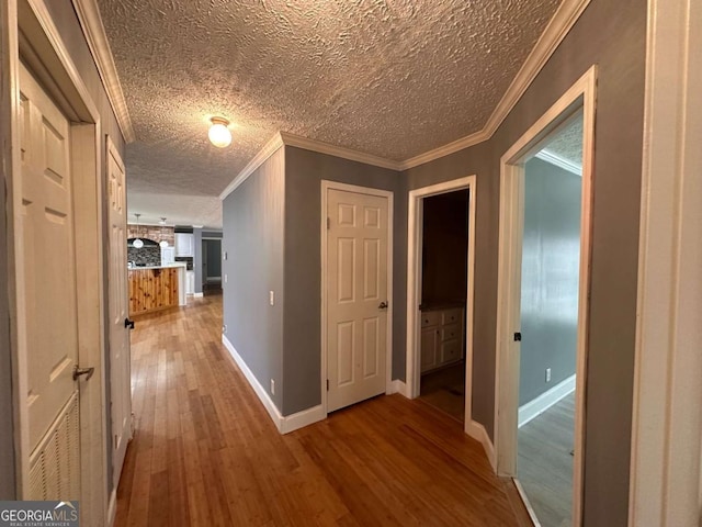 hall with baseboards, a textured ceiling, wood-type flooring, and crown molding