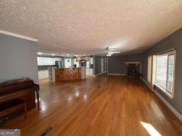 unfurnished living room with hardwood / wood-style flooring, a fireplace, a ceiling fan, baseboards, and ornamental molding