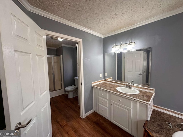 bathroom featuring toilet, wood finished floors, crown molding, vanity, and a shower stall