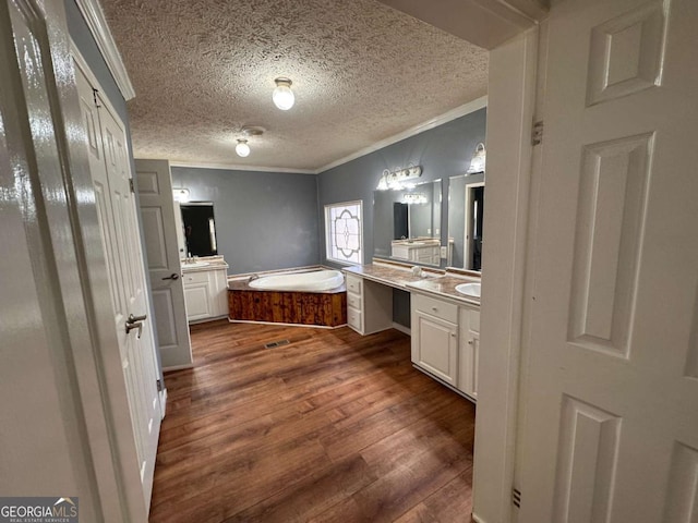 bathroom with a garden tub, two vanities, ornamental molding, a textured ceiling, and wood finished floors