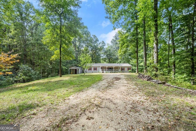 ranch-style home featuring a front yard, driveway, and a wooded view