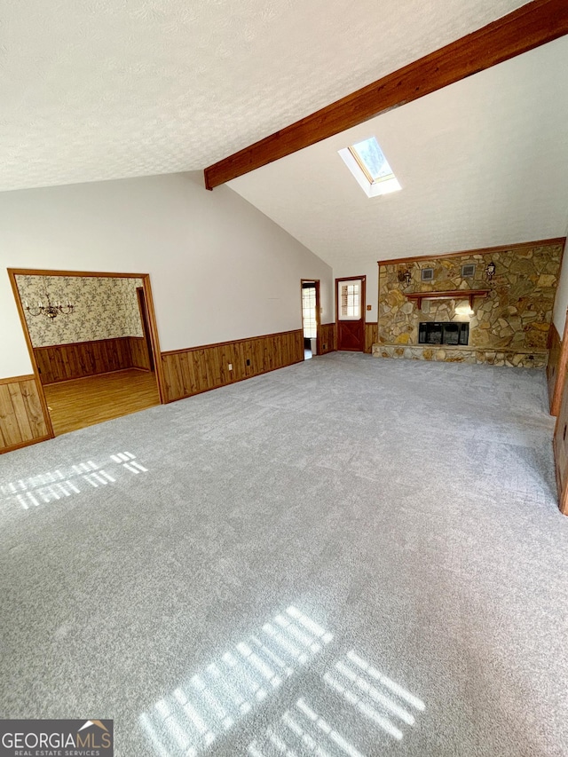 unfurnished living room featuring a wainscoted wall, lofted ceiling with skylight, a textured ceiling, and wooden walls