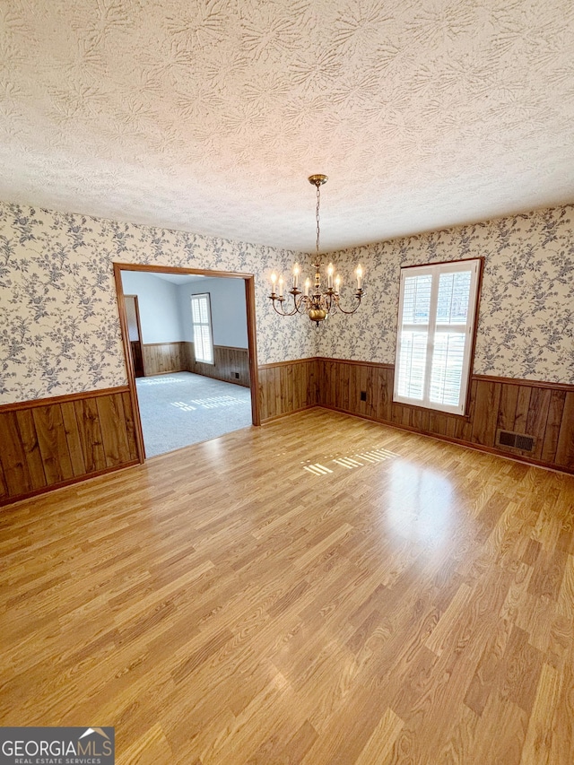 unfurnished dining area with wood finished floors, a wainscoted wall, a textured ceiling, and wallpapered walls