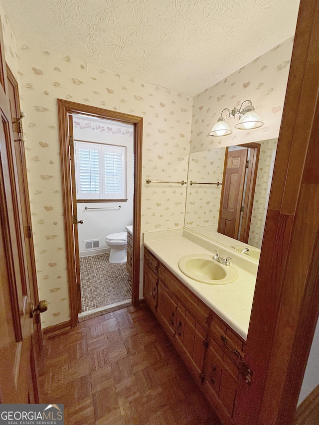 bathroom with a textured ceiling, vanity, toilet, and wallpapered walls