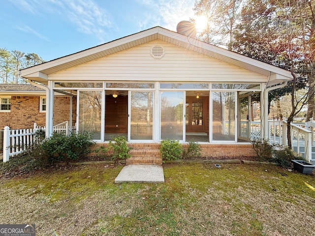 rear view of property with a sunroom, a yard, fence, and brick siding