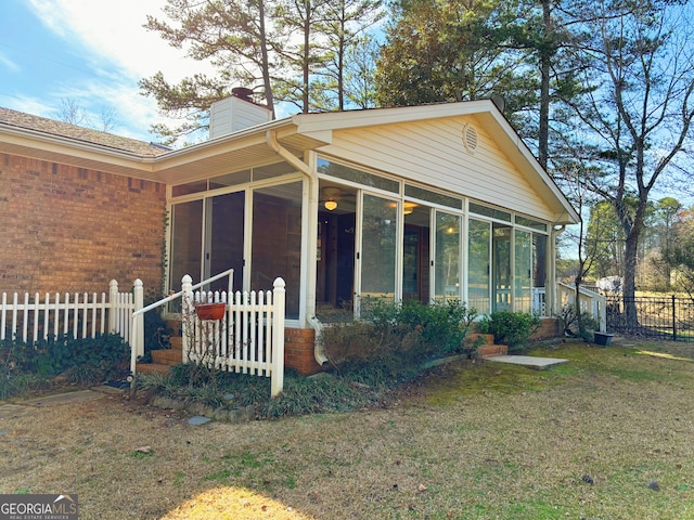 exterior space featuring a sunroom, a chimney, fence, a front lawn, and brick siding