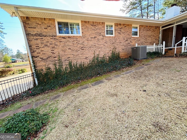 view of side of property featuring brick siding, a chimney, and central AC unit