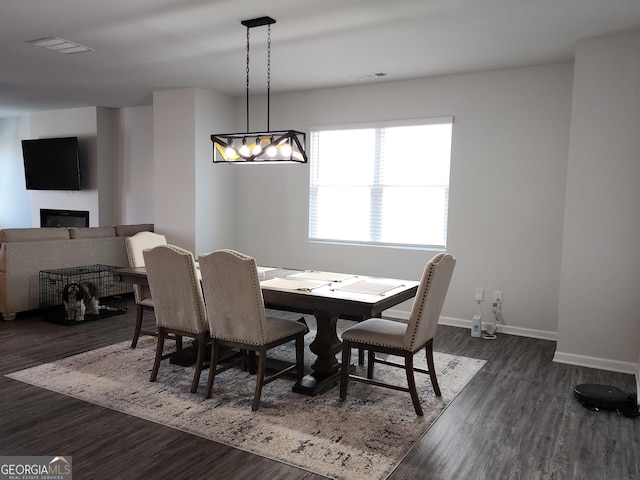 dining space with a glass covered fireplace, dark wood finished floors, visible vents, and baseboards