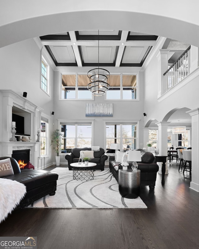 living room with a healthy amount of sunlight, dark wood-style floors, a lit fireplace, and decorative columns