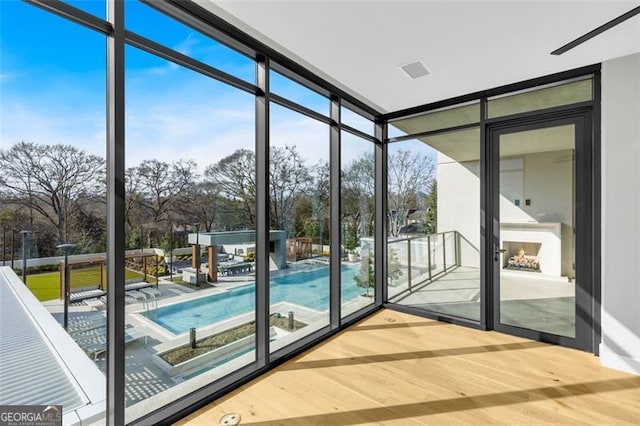 doorway to outside featuring a lit fireplace, expansive windows, and wood finished floors