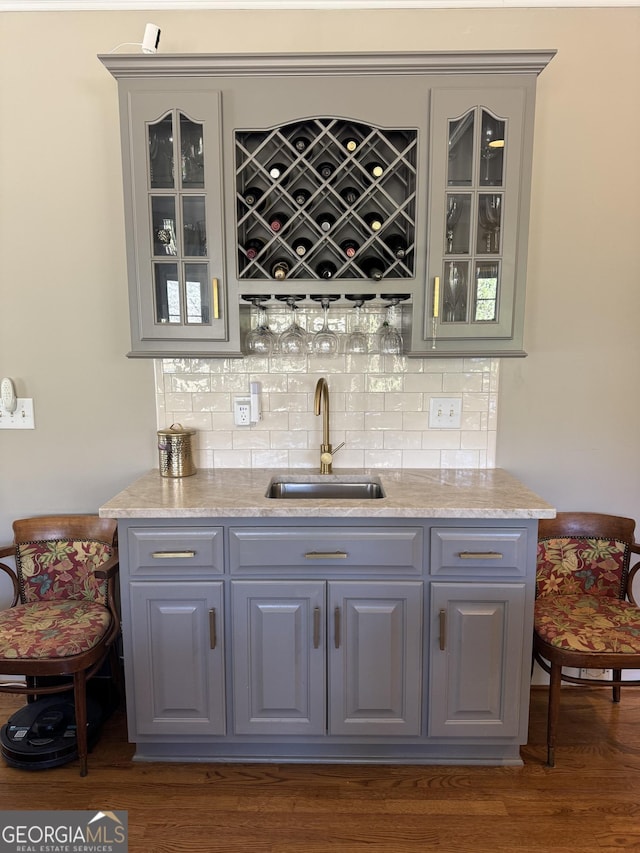 bar with dark wood-type flooring, backsplash, a sink, and wet bar