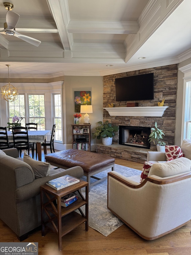 living room featuring coffered ceiling, ornamental molding, beamed ceiling, wood finished floors, and a stone fireplace