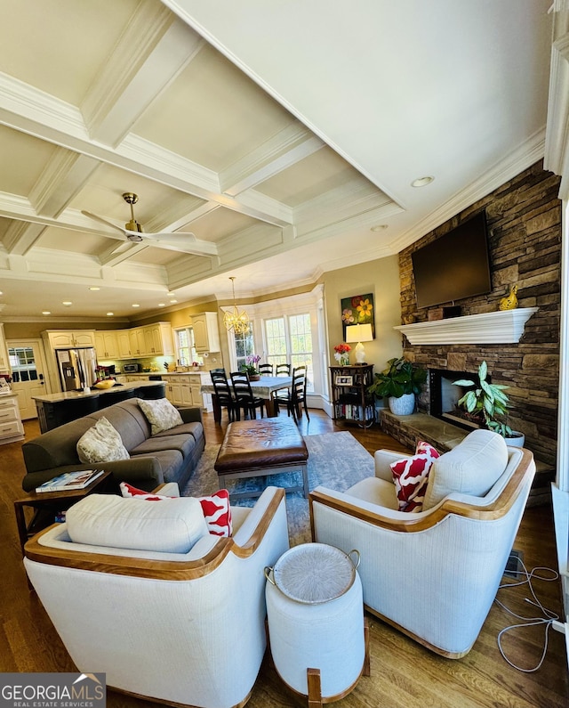 living area with coffered ceiling, dark wood-type flooring, crown molding, a stone fireplace, and beam ceiling