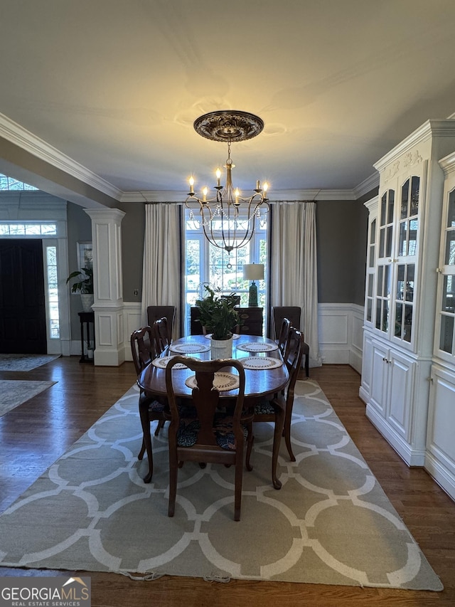 dining room with crown molding, wood finished floors, decorative columns, and an inviting chandelier