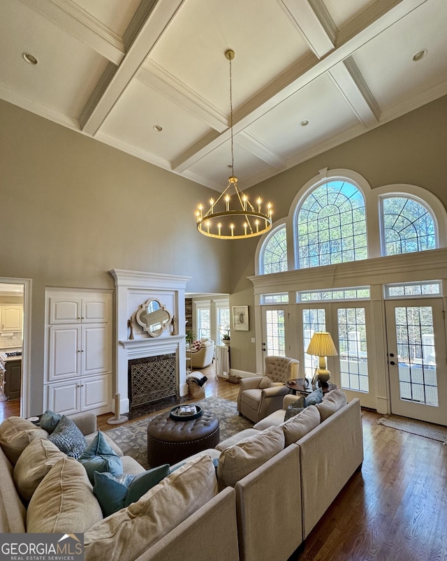 living room with a notable chandelier, a fireplace, coffered ceiling, and dark wood-style flooring