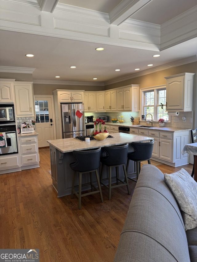 kitchen with appliances with stainless steel finishes, white cabinets, a sink, wood finished floors, and a kitchen breakfast bar