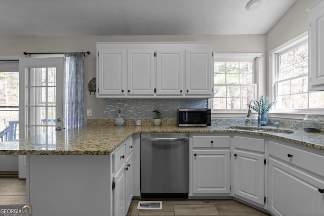 kitchen with a peninsula, white cabinetry, appliances with stainless steel finishes, and a sink