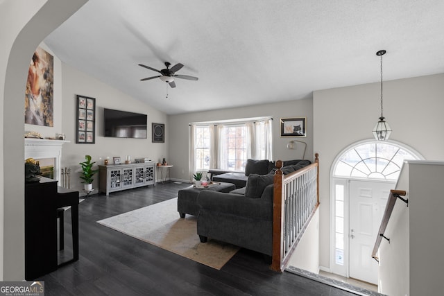 living area featuring dark wood finished floors, a ceiling fan, lofted ceiling, a textured ceiling, and a fireplace