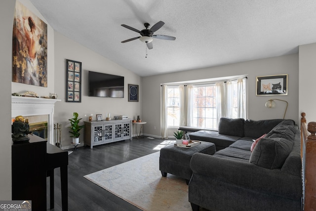 living area with dark wood-style flooring, a ceiling fan, a glass covered fireplace, vaulted ceiling, and a textured ceiling