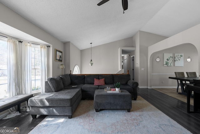 living area with arched walkways, lofted ceiling, a textured ceiling, wood finished floors, and baseboards