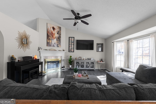 living room featuring lofted ceiling, ceiling fan, a textured ceiling, wood finished floors, and a fireplace with flush hearth