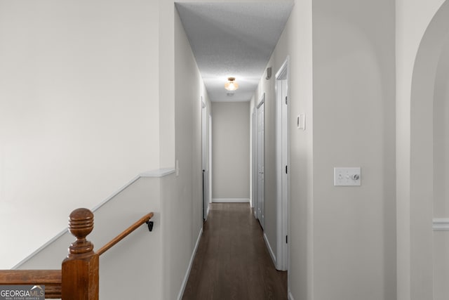 hall with a textured ceiling, dark wood-style floors, an upstairs landing, and baseboards