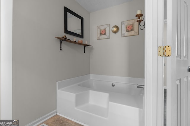 bathroom with a textured ceiling, a garden tub, and baseboards