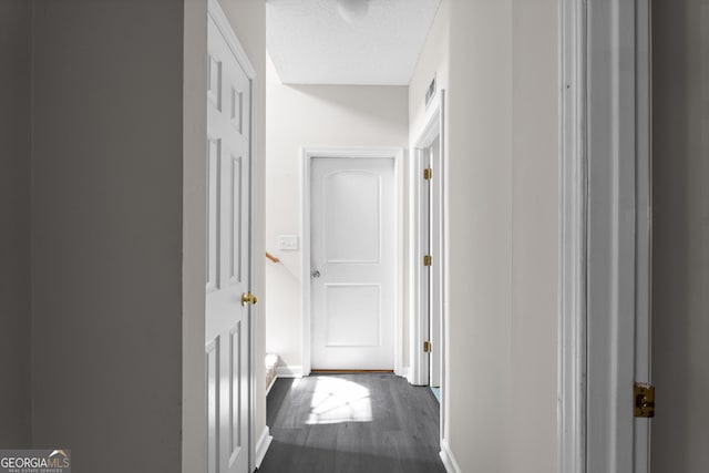 hall featuring a textured ceiling, baseboards, and dark wood-type flooring