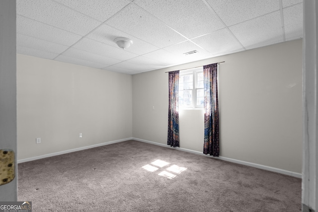 spare room with carpet floors, baseboards, visible vents, and a drop ceiling