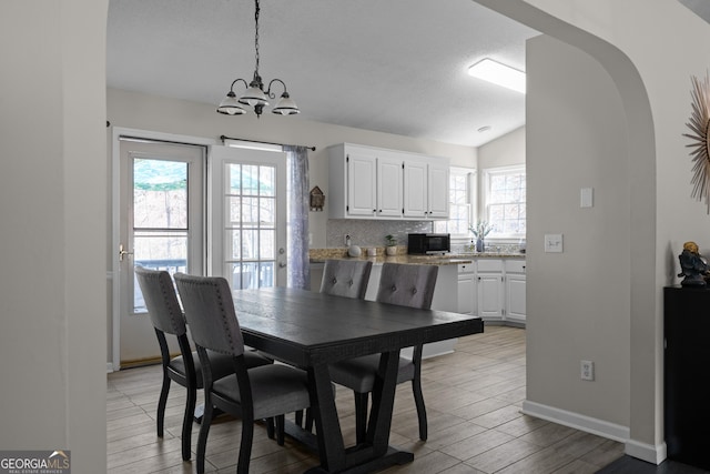 dining room featuring light wood finished floors, arched walkways, vaulted ceiling, and a notable chandelier