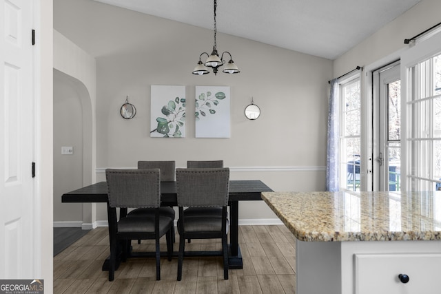 dining area featuring lofted ceiling, wood finish floors, arched walkways, and a notable chandelier