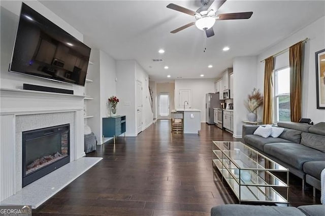 living room featuring recessed lighting, dark wood-type flooring, visible vents, built in features, and a glass covered fireplace