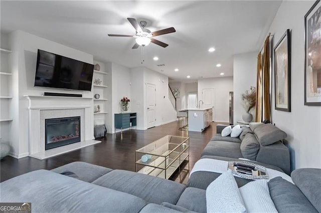 living room with baseboards, a glass covered fireplace, dark wood-style floors, built in shelves, and recessed lighting