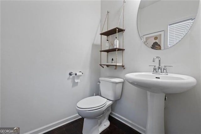 half bath with a sink, toilet, baseboards, and wood finished floors