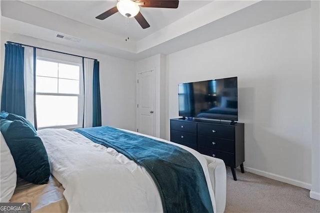 bedroom with light carpet, a ceiling fan, visible vents, baseboards, and a tray ceiling