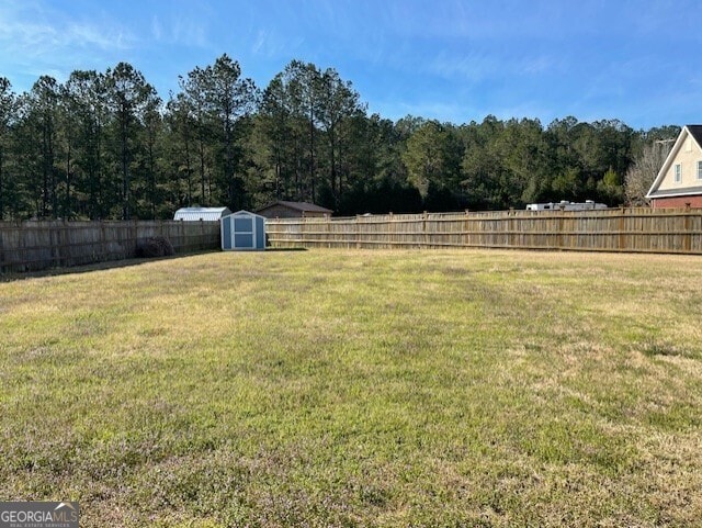 view of yard featuring a fenced backyard, a storage unit, a wooded view, and an outbuilding