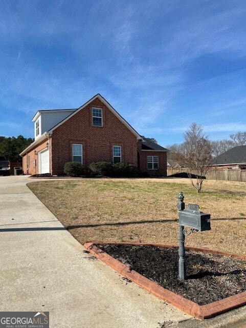 view of property exterior with a yard, fence, concrete driveway, and brick siding