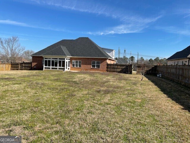 back of property featuring a fenced backyard, a yard, and brick siding