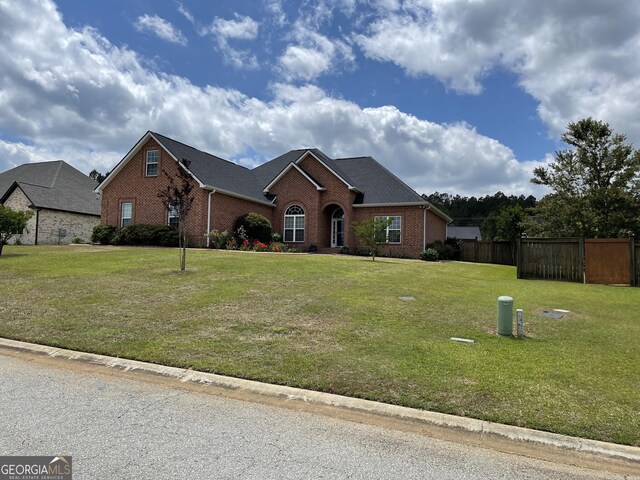 ranch-style house featuring brick siding, a front lawn, and fence