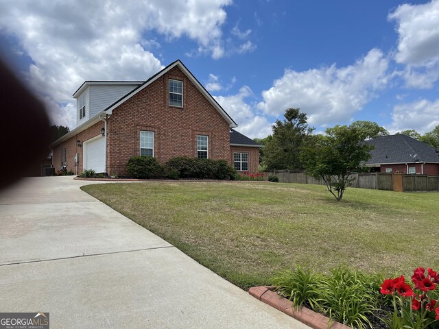view of home's exterior with a yard, a garage, brick siding, fence, and concrete driveway