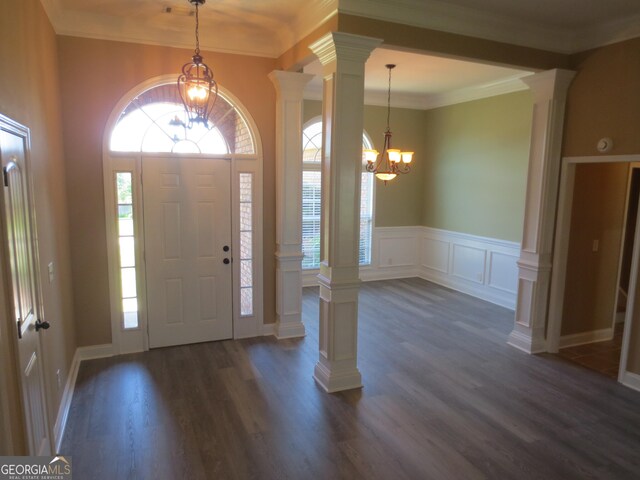 empty room featuring an inviting chandelier, crown molding, wood finished floors, and ornate columns