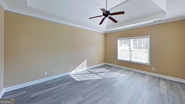 empty room with baseboards, visible vents, a raised ceiling, and wood finished floors