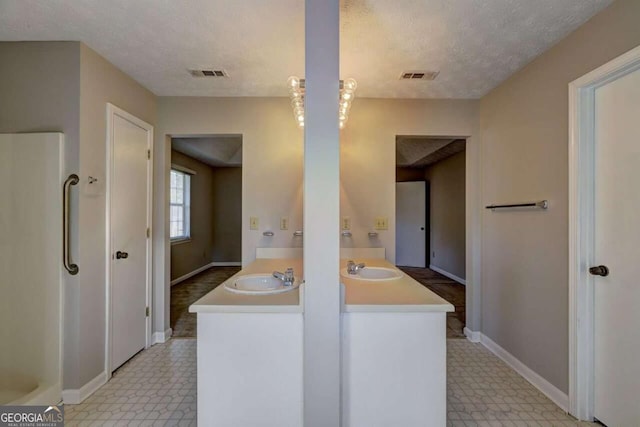 bathroom featuring double vanity, a textured ceiling, visible vents, and a sink